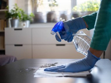 Yüzeyde ev temizliği antibakteriyel sprey sprey spreyi sıkarak COVID-19 'a karşı dezenfekte ederek mavi eldiven takarak yayılıyor. Hastanelerde ve kamusal alanlarda yüzeylerin temizlenmesi.