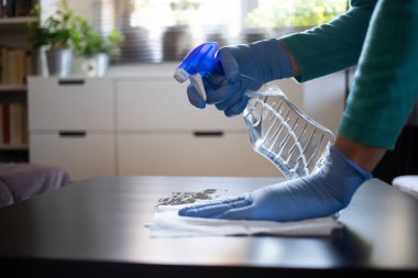 Yüzeyde ev temizliği antibakteriyel sprey sprey spreyi sıkarak COVID-19 'a karşı dezenfekte ederek mavi eldiven takarak yayılıyor. Hastanelerde ve kamusal alanlarda yüzeylerin temizlenmesi.