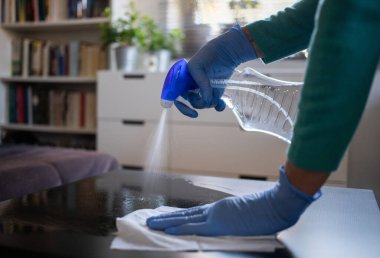 Yüzeyde ev temizliği antibakteriyel sprey sprey spreyi sıkarak COVID-19 'a karşı dezenfekte ederek mavi eldiven takarak yayılıyor. Hastanelerde ve kamusal alanlarda yüzeylerin temizlenmesi.