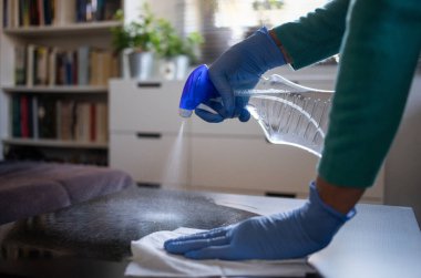 Yüzeyde ev temizliği antibakteriyel sprey sprey spreyi sıkarak COVID-19 'a karşı dezenfekte ederek mavi eldiven takarak yayılıyor. Hastanelerde ve kamusal alanlarda yüzeylerin temizlenmesi.