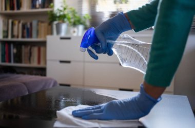 Yüzeyde ev temizliği antibakteriyel sprey sprey spreyi sıkarak COVID-19 'a karşı dezenfekte ederek mavi eldiven takarak yayılıyor. Hastanelerde ve kamusal alanlarda yüzeylerin temizlenmesi.