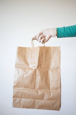Market teslimatçısı COVID-19 Coronavirus önlemleri için mavi eldiven takan bir kağıt torba verdi..