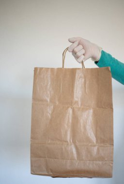 Market teslimatçısı COVID-19 Coronavirus önlemleri için mavi eldiven takan bir kağıt torba verdi..