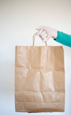 Market teslimatçısı COVID-19 Coronavirus önlemleri için mavi eldiven takan bir kağıt torba verdi..