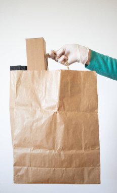 Market teslimatçısı COVID-19 Coronavirus önlemleri için mavi eldiven takan bir kağıt torba verdi..