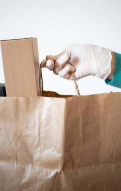 Market teslimatçısı COVID-19 Coronavirus önlemleri için mavi eldiven takan bir kağıt torba verdi..