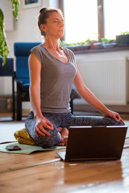 Evde yoga yapan bir kadın dizüstü bilgisayardan video izliyor.