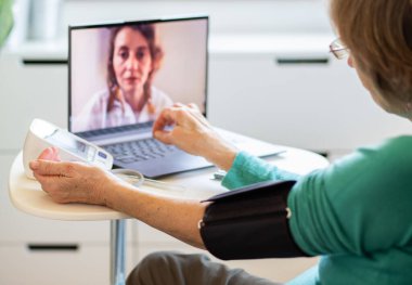 Teletıp konsepti. Yaşlı bir kadın doktoruyla internetten konuşuyor ve tansiyonunu ölçüyor.