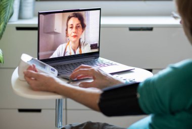 Teletıp konsepti. Yaşlı bir kadın doktoruyla internetten konuşuyor ve tansiyonunu ölçüyor.