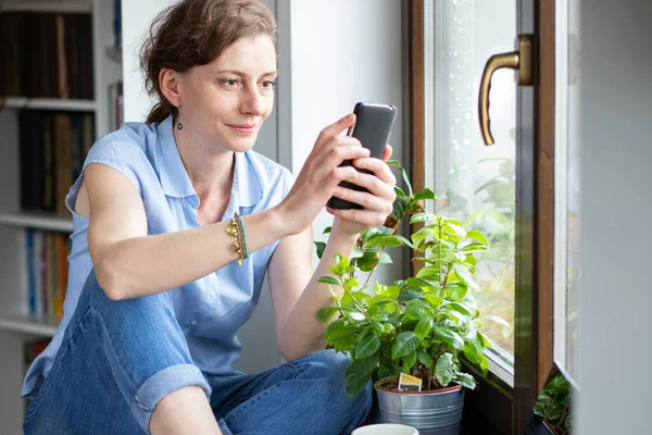 Lycklig Kvinna Använder Smartphone Hemma Genom Fönstret Sociala Medier Anslutning — Stockfoto