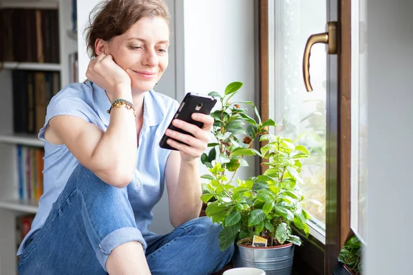 Mulher Feliz Usando Smartphone Casa Pela Janela Conexão Mídia Social — Fotografia de Stock