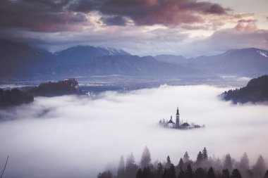 Sisli bir sabahta, Bled Blejsko Jezero Gölü 'nün muhteşem manzarası. Küçük bir adada Maria' nın Hacı Kilisesi ve arka planda Kanlı Kale ve Julian Alps.