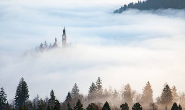 Sisli bir sabahta, Bled Blejsko Jezero Gölü 'nün muhteşem manzarası. Küçük bir adada Maria' nın Hacı Kilisesi ve arka planda Kanlı Kale ve Julian Alps.