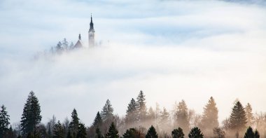 Sisli bir sabahta, Bled Blejsko Jezero Gölü 'nün muhteşem manzarası. Küçük bir adada Maria' nın Hacı Kilisesi ve arka planda Kanlı Kale ve Julian Alps.