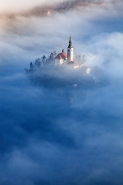 Sisli bir sabahta, Bled Blejsko Jezero Gölü 'nün muhteşem manzarası. Küçük bir adada Maria' nın Hacı Kilisesi ve arka planda Kanlı Kale ve Julian Alps.
