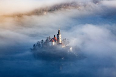 Sisli bir sabahta, Bled Blejsko Jezero Gölü 'nün muhteşem manzarası. Küçük bir adada Maria' nın Hacı Kilisesi ve arka planda Kanlı Kale ve Julian Alps.