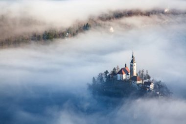 Sisli bir sabahta, Bled Blejsko Jezero Gölü 'nün muhteşem manzarası. Küçük bir adada Maria' nın Hacı Kilisesi ve arka planda Kanlı Kale ve Julian Alps.