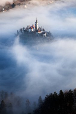 Sisli bir sabahta, Bled Blejsko Jezero Gölü 'nün muhteşem manzarası. Küçük bir adada Maria' nın Hacı Kilisesi ve arka planda Kanlı Kale ve Julian Alps.