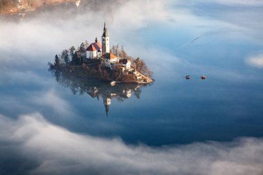 Sisli bir sabahta, Bled Blejsko Jezero Gölü 'nün muhteşem manzarası. Küçük bir adada Maria' nın Hacı Kilisesi ve arka planda Kanlı Kale ve Julian Alps.