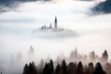 Sisli bir sabahta, Bled Blejsko Jezero Gölü 'nün muhteşem manzarası. Küçük bir adada Maria' nın Hacı Kilisesi ve arka planda Kanlı Kale ve Julian Alps.