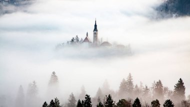 Sisli bir sabahta, Bled Blejsko Jezero Gölü 'nün muhteşem manzarası. Küçük bir adada Maria' nın Hacı Kilisesi ve arka planda Kanlı Kale ve Julian Alps.