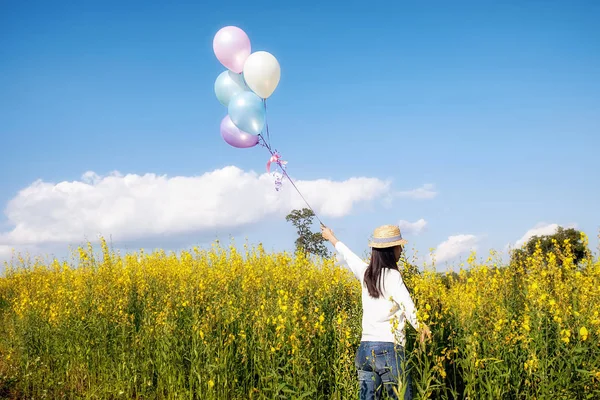 Mano de niña sosteniendo globos multicolores realizados en el jardín de flores amarillas. Concepto relajante. Efecto filtro retro, enfoque selectivo . — Foto de Stock