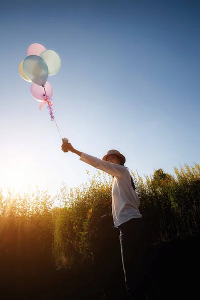 Mano de niña sosteniendo globos multicolores realizados en el jardín de flores amarillas. Concepto relajante. Efecto filtro retro, enfoque selectivo — Foto de Stock