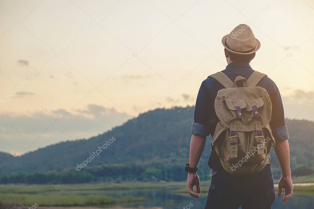 Hipster young man with backpack enjoying sunset on peak mountain. Tourist traveler on background valley landscape view mock-up.Retro filter effect, selective focus.