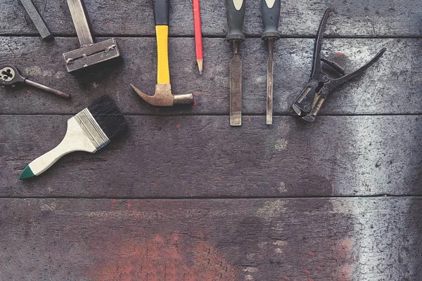 Tono vintage del equipo en escritorio de madera con el hombre trabajando en el fondo del taller. Efecto filtro retro, poca luz, enfoque selectivo . — Foto de Stock