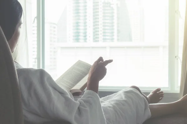 Hermosa mujer asiática sentada en la cama con una taza de café y leyendo un libro. Mañana con un libro y una taza de café. Concepto relajante. Efecto filtro retro, enfoque suave, enfoque selectivo — Foto de Stock
