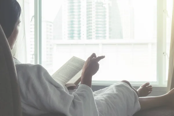 Beautiful asian female sitting on the bed with a cup of coffee and reading a book. Morning with a book and cup of coffee. Relaxing concept. Retro filter effect,soft focus,selective focus — Stock Photo, Image