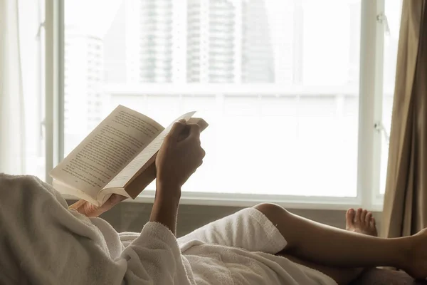 Красивая азиатская женщина сидит на кровати с чашкой кофе и читает книгу. Утро с книгой и чашкой кофе. Расслабляющая концепция. Эффект ретро-фильтра, мягкая фокусировка, избирательная фокусировка — стоковое фото