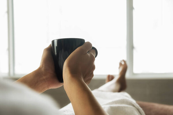 Beautiful asian female sitting on the bed with a cup of coffee and reading a book. Morning with a book and cup of coffee. Relaxing concept. Retro filter effect,soft focus,selective focus