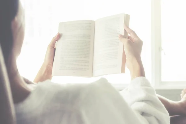 Hermosa mujer asiática sentada en la cama con una taza de café y leyendo un libro. Mañana con un libro y una taza de café. Concepto relajante. Efecto filtro retro, enfoque suave, enfoque selectivo — Foto de Stock