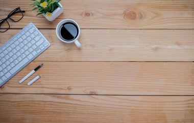 Ofis resepsiyon masası kalem, defter, fincan kahve ve çiçek üzerinde klavye ile. Kopya alanı (seçici odak ile Üstten Görünüm).