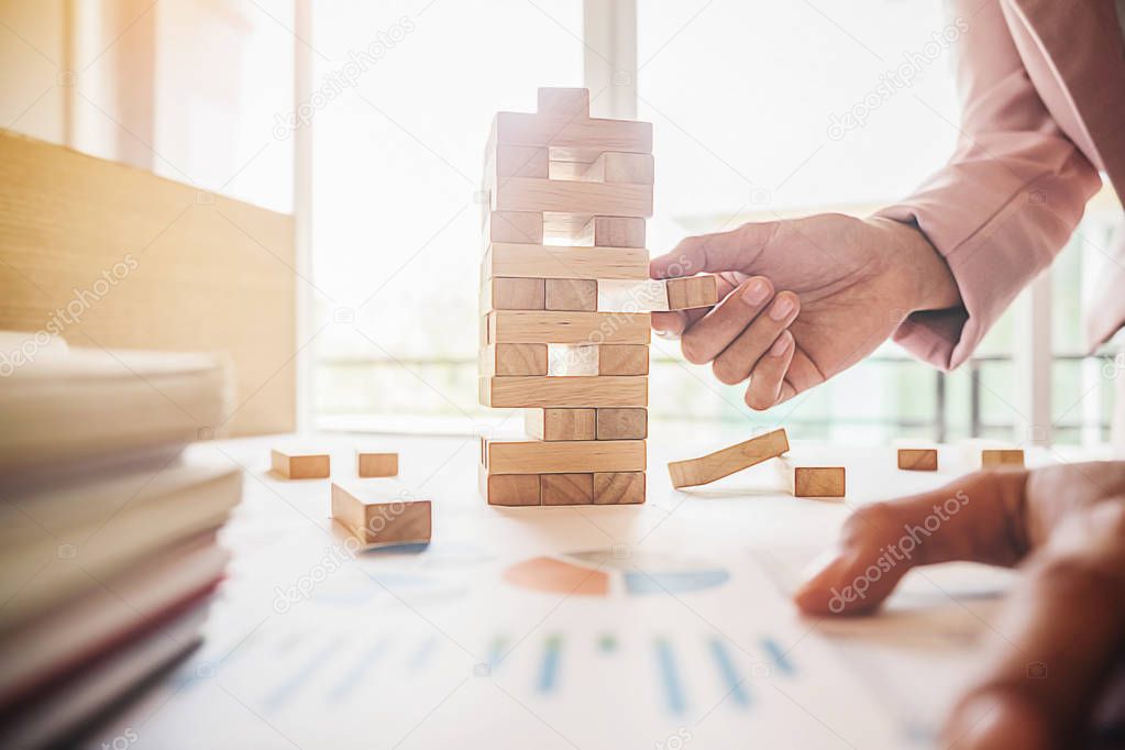 Hand of business man planning, risk and strategy in business.Businessman gambling placing wooden block on a tower.