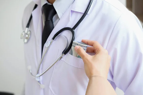 Doctor with white gown and stethoscope with a wad of dollar ban