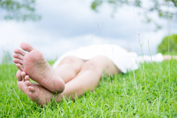 Счастливая женщина лежит на зеленом травяном лугу на вершине скалы, наслаждаясь солнцем на ее лице.
