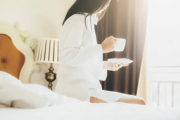 Beautiful asian woman holding a cup of coffee on the bed with mo — Stock Photo, Image