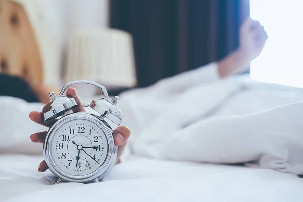 Роздратована молода жінка відкладає будильник вранці — стокове фото