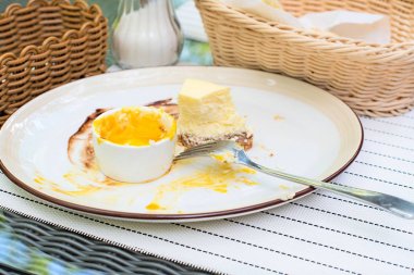 Büyük beyaz çanak, mango soslu krem peynirli kek. Parlak bokeh arka plan. Çatal bıçak takımı, beyaz peçeteler, kahve fincanı, şekerlik, hasır sandalyeleri sepetle. Tatlı. Vişne suyu