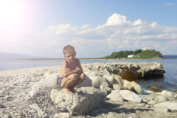 Мальчик сидит среди камней на берегу моря — стоковое фото