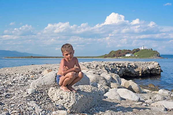 Мальчик сидит среди камней на берегу моря — стоковое фото