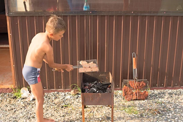 Chłopiec jest grillowania mięsa na grilla. — Zdjęcie stockowe