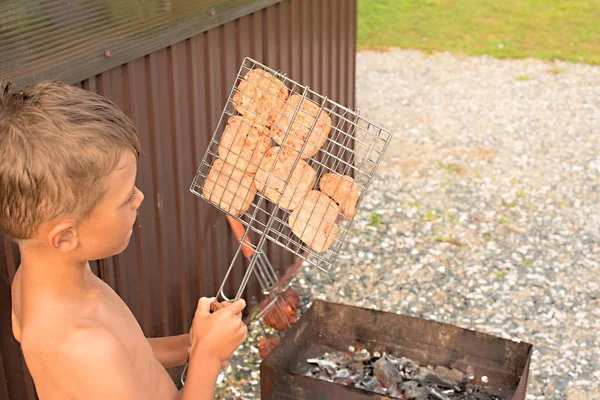 Il ragazzo sta grigliando carne su un barbecue . — Foto Stock
