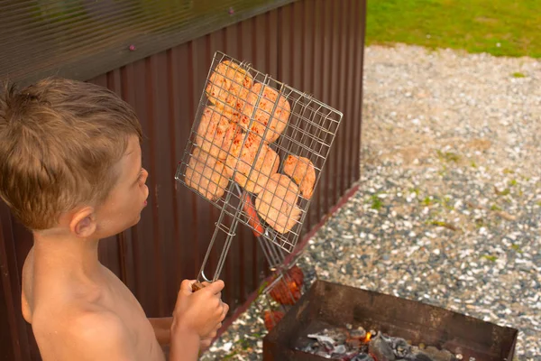 Il ragazzo sta grigliando carne su un barbecue . — Foto Stock