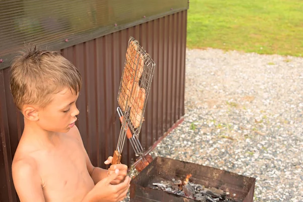 Le garçon fait griller de la viande sur un barbecue . — Photo