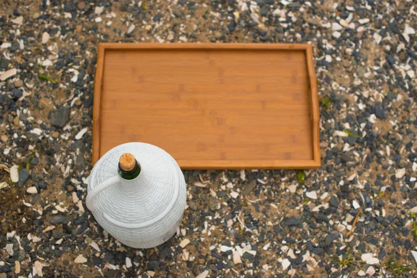 Een grote wijn kruik en een houten dienblad op een achtergrond zee pebbles. — Stockfoto