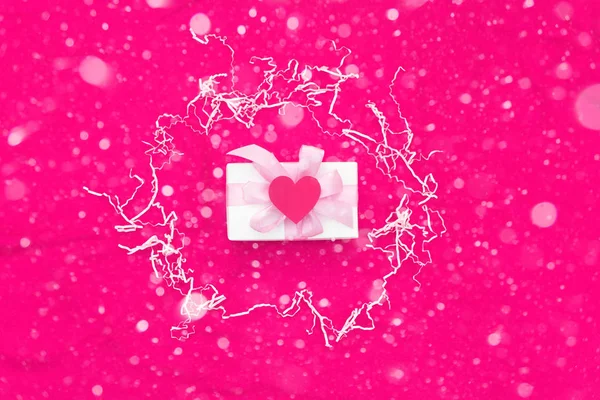 Una caja de regalo atada con cinta de color satén sobre un fondo rojo un corazón rojo . — Foto de Stock