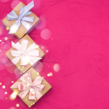 Üç hediye kutuları ile saten renkli şerit pembe bir arka plan üzerinde kırmızı bir kalp bağlı.